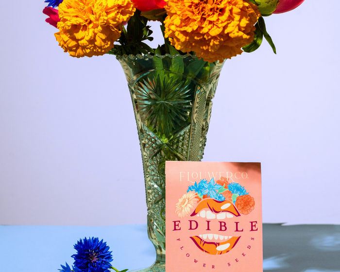 A bouquet of edible flowers in a crystal vase next to a seed packet