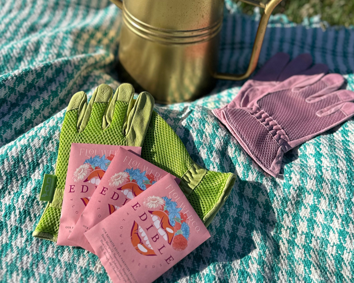 Flouwer Co. edible seed packets, green and pink mesh gardening gloves, and a brass watering can