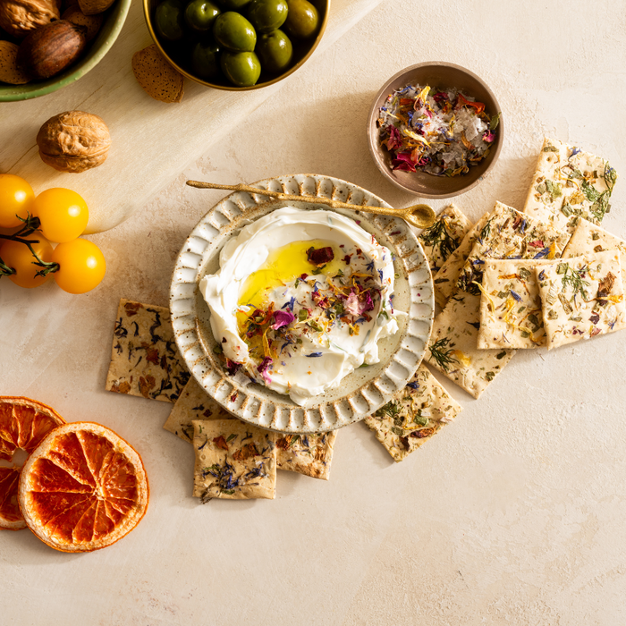 Artisanal floral crackers served around whipped feta dip with olive oil, dried petals, olives, walnuts, and dried citrus