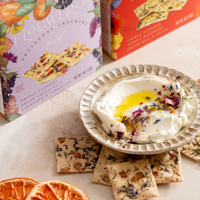 Box of floral crackers next to a bowl of labneh dip garnished with olive oil and flower petals