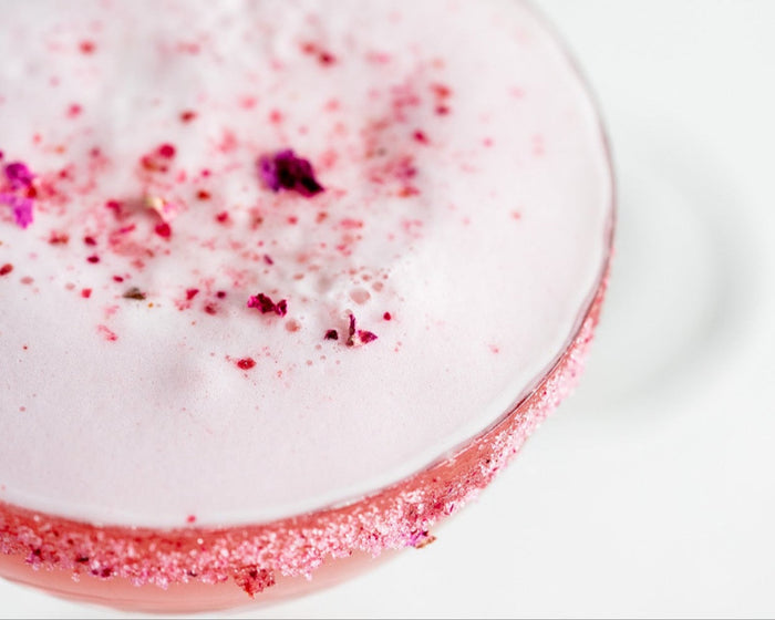 Blushing Rose" cocktail, featuring a frothy top garnished with dried rose petals